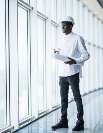 Young Afro-American engineer with blue prints in front of panoramic windows in office